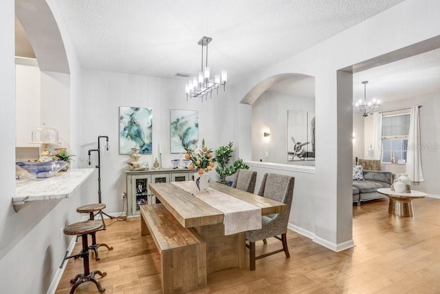 dining space with light wood-type flooring, a textured ceiling, and a chandelier