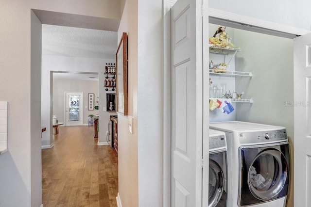 clothes washing area featuring washer and clothes dryer, a textured ceiling, and light hardwood / wood-style flooring