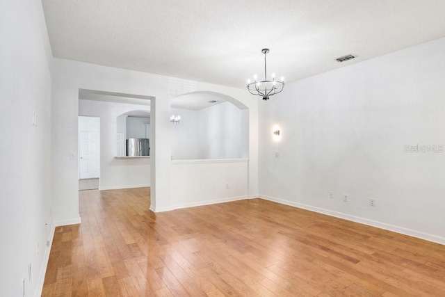 unfurnished room featuring a chandelier, light wood-type flooring, visible vents, and baseboards