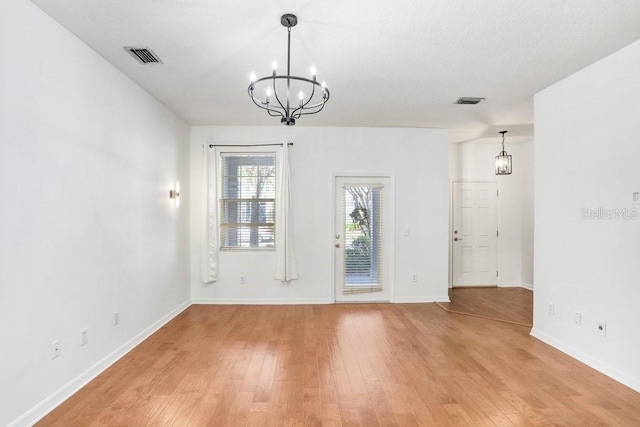 interior space with an inviting chandelier, light wood-style flooring, visible vents, and baseboards