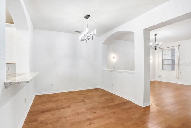 unfurnished dining area with a chandelier, wood finished floors, visible vents, and baseboards