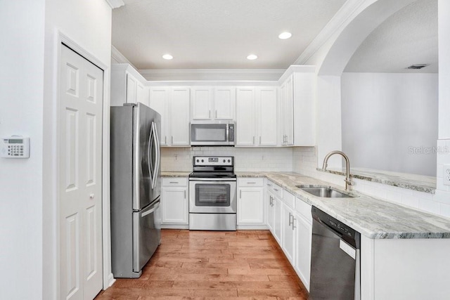 kitchen featuring arched walkways, decorative backsplash, stainless steel appliances, light wood-type flooring, and a sink