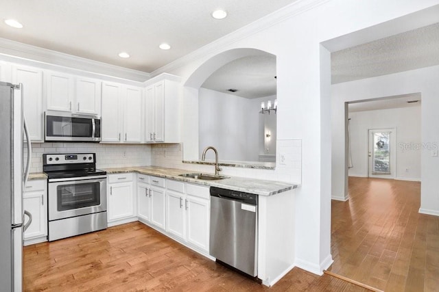 kitchen with decorative backsplash, appliances with stainless steel finishes, white cabinetry, a sink, and light wood-type flooring