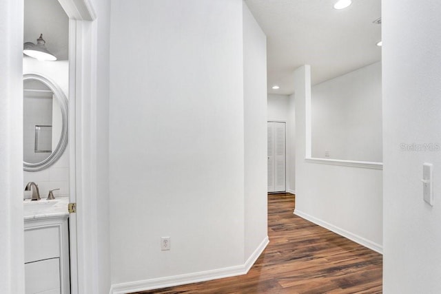 corridor featuring a sink, recessed lighting, wood finished floors, and baseboards