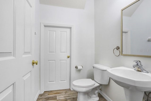 half bath featuring toilet, a sink, baseboards, and wood finished floors