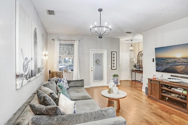 living room featuring light wood-type flooring, baseboards, visible vents, and a textured ceiling