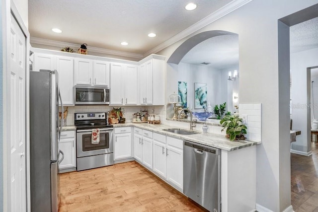 kitchen featuring arched walkways, stainless steel appliances, a sink, light wood finished floors, and tasteful backsplash