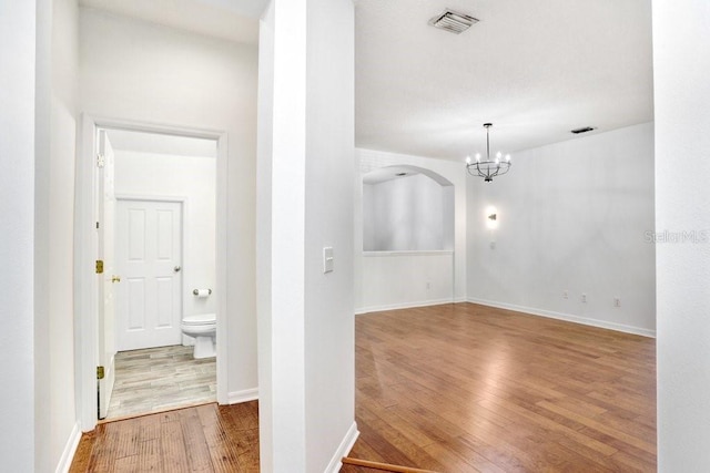 spare room with baseboards, visible vents, arched walkways, and wood finished floors