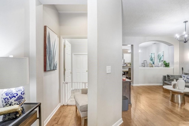 hall featuring arched walkways, a textured ceiling, a notable chandelier, baseboards, and light wood-type flooring