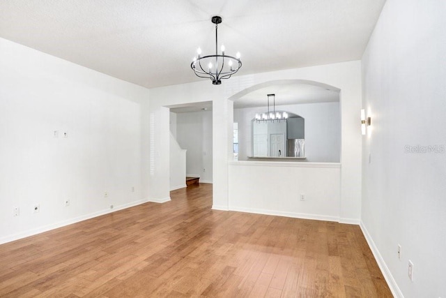 unfurnished room with a chandelier, light wood-type flooring, and baseboards