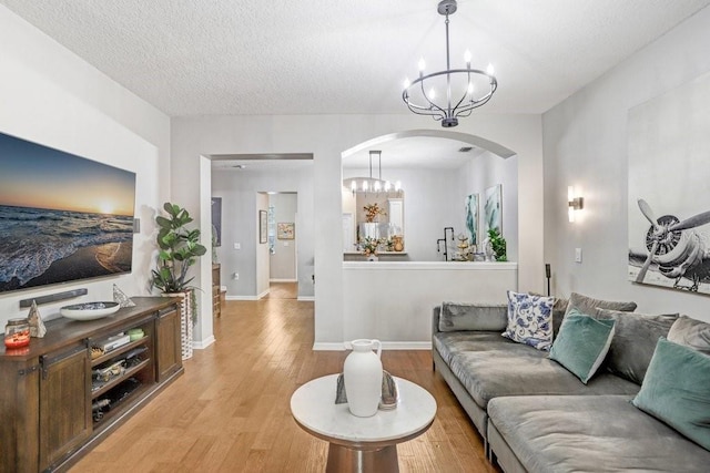 living room featuring a chandelier, arched walkways, light wood-style flooring, and baseboards