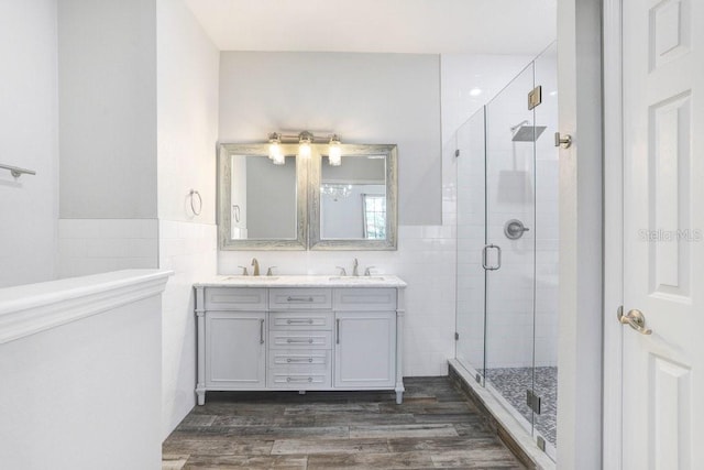 full bath with a stall shower, a sink, tile walls, and wood finished floors