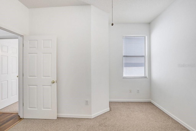 spare room with baseboards, a textured ceiling, and light colored carpet