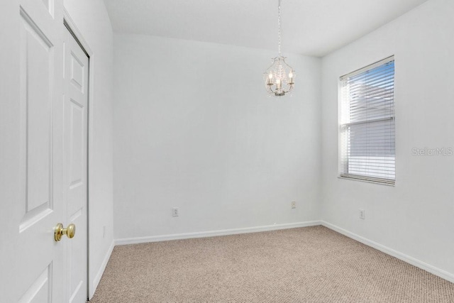 spare room featuring baseboards, a chandelier, and light colored carpet