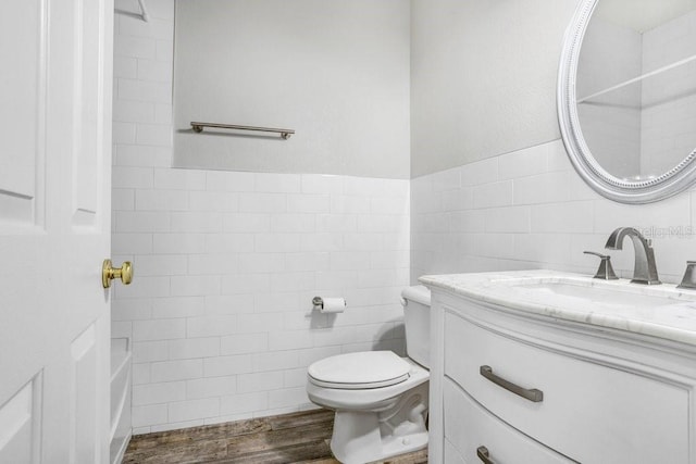 bathroom featuring toilet, a wainscoted wall, wood finished floors, vanity, and tile walls