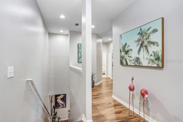 corridor with recessed lighting, wood finished floors, visible vents, an upstairs landing, and baseboards