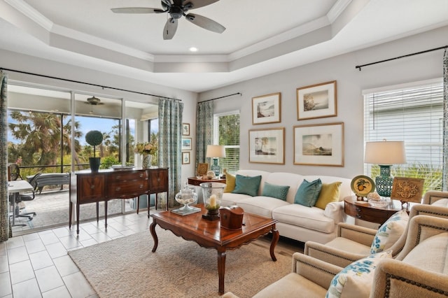 tiled living room with ceiling fan, a tray ceiling, and ornamental molding