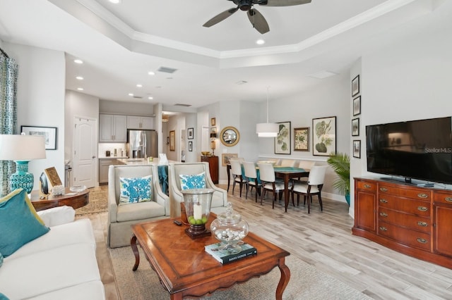 living room with ceiling fan, crown molding, a raised ceiling, and light wood-type flooring