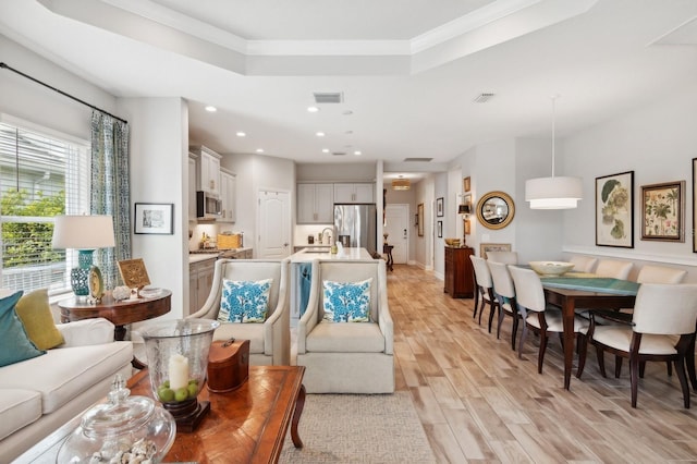 living room featuring a raised ceiling, sink, ornamental molding, and light hardwood / wood-style flooring