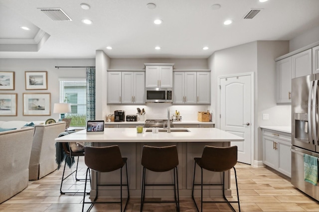 kitchen featuring white cabinetry, stainless steel appliances, an island with sink, a kitchen breakfast bar, and backsplash