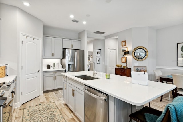 kitchen with tasteful backsplash, a kitchen bar, sink, a kitchen island with sink, and stainless steel appliances