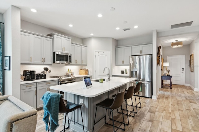 kitchen with appliances with stainless steel finishes, a kitchen bar, sink, backsplash, and a kitchen island with sink