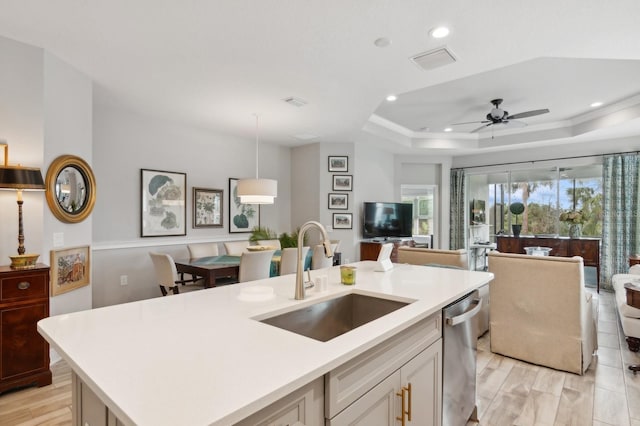 kitchen featuring pendant lighting, a tray ceiling, sink, stainless steel dishwasher, and a center island with sink