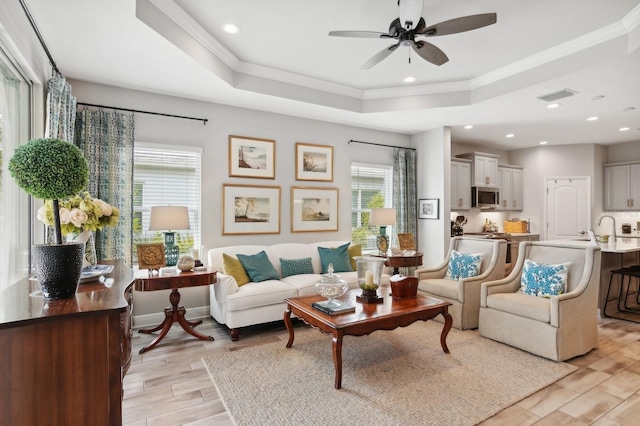 living room with ceiling fan, crown molding, a raised ceiling, and sink