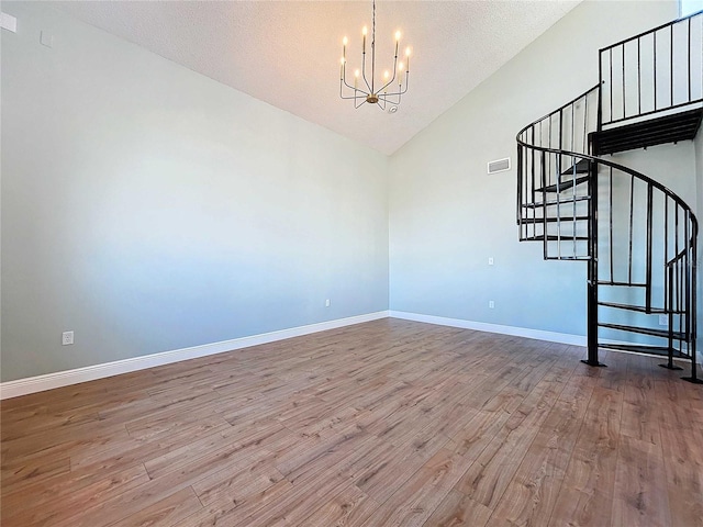 spare room featuring hardwood / wood-style flooring, a textured ceiling, high vaulted ceiling, and an inviting chandelier