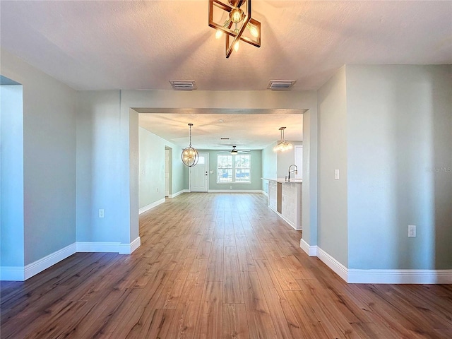 unfurnished living room with a textured ceiling, ceiling fan with notable chandelier, wood-type flooring, and sink