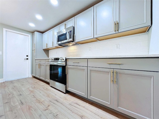 kitchen with light stone countertops, decorative backsplash, gray cabinetry, stainless steel appliances, and light hardwood / wood-style floors