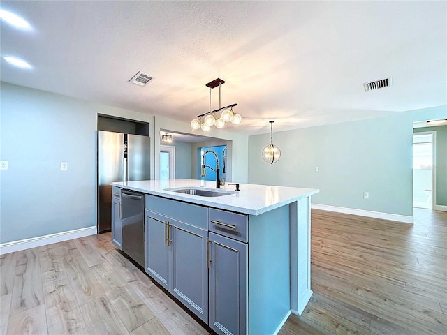 kitchen featuring sink, an island with sink, decorative light fixtures, light hardwood / wood-style floors, and stainless steel appliances