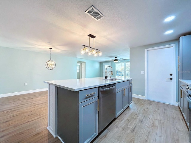 kitchen featuring dishwasher, sink, light hardwood / wood-style floors, decorative light fixtures, and a kitchen island with sink