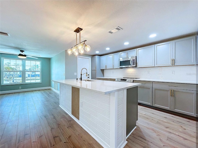 kitchen with sink, stainless steel appliances, tasteful backsplash, pendant lighting, and ceiling fan with notable chandelier