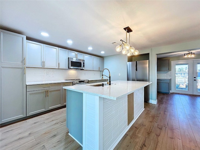 kitchen featuring sink, tasteful backsplash, light hardwood / wood-style flooring, decorative light fixtures, and appliances with stainless steel finishes