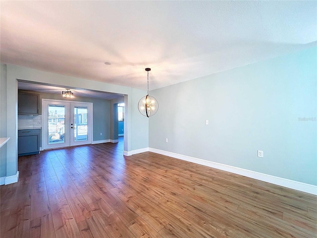 empty room with a notable chandelier, dark hardwood / wood-style flooring, and french doors