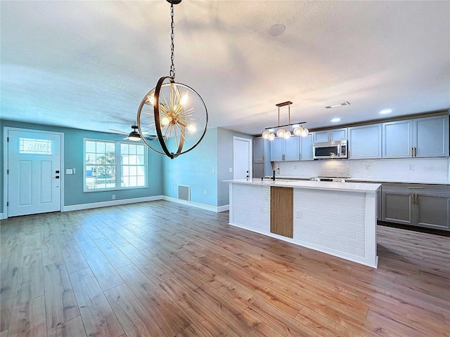 kitchen featuring decorative light fixtures, backsplash, a center island with sink, and light hardwood / wood-style floors