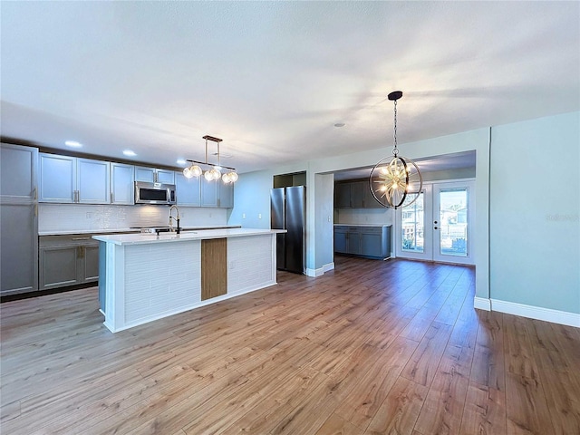 kitchen with hanging light fixtures, stainless steel appliances, tasteful backsplash, light hardwood / wood-style flooring, and a kitchen island with sink