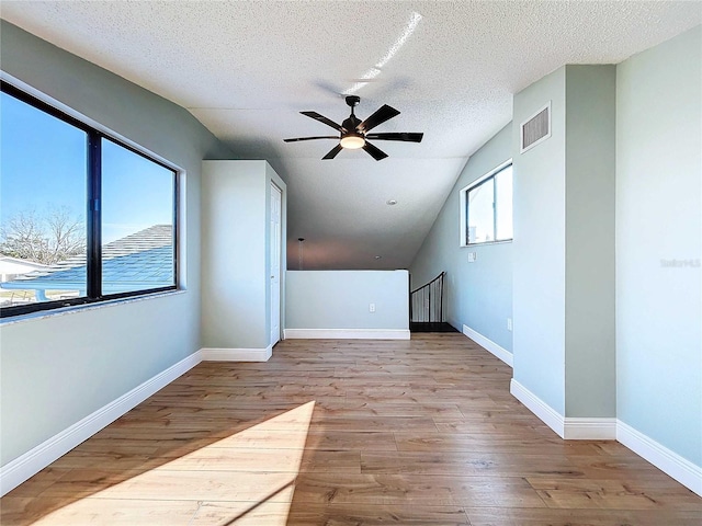 additional living space featuring a textured ceiling, light hardwood / wood-style floors, and vaulted ceiling