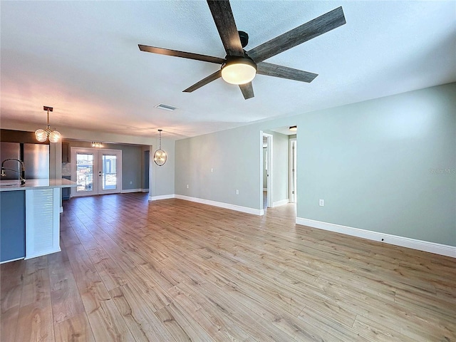 unfurnished living room with light hardwood / wood-style flooring, ceiling fan with notable chandelier, french doors, and sink