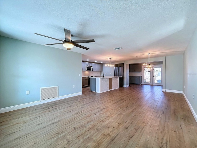 unfurnished living room with french doors, ceiling fan with notable chandelier, sink, light wood-type flooring, and a textured ceiling