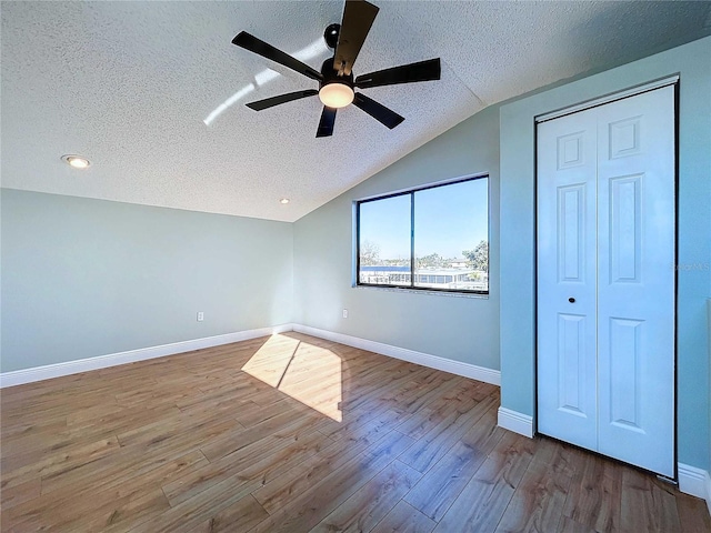 unfurnished bedroom with hardwood / wood-style flooring, ceiling fan, a textured ceiling, and vaulted ceiling