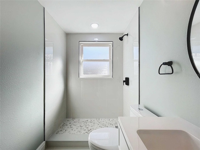 bathroom featuring a tile shower, vanity, and toilet