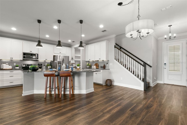 kitchen featuring appliances with stainless steel finishes, white cabinetry, hanging light fixtures, a notable chandelier, and a center island with sink