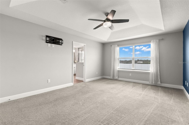 empty room with a raised ceiling, carpet, a textured ceiling, and ceiling fan