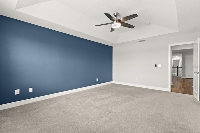 empty room with a tray ceiling, ceiling fan, and carpet