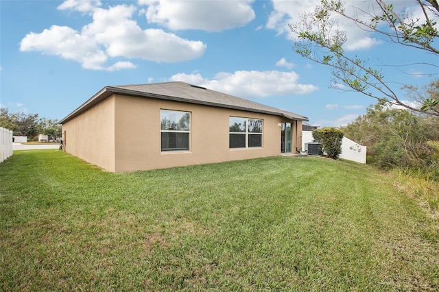 rear view of property featuring central AC and a lawn