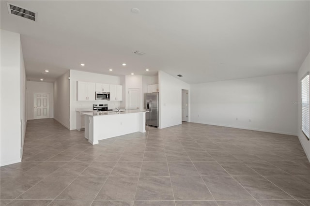 kitchen with light tile patterned flooring, appliances with stainless steel finishes, white cabinetry, and an island with sink