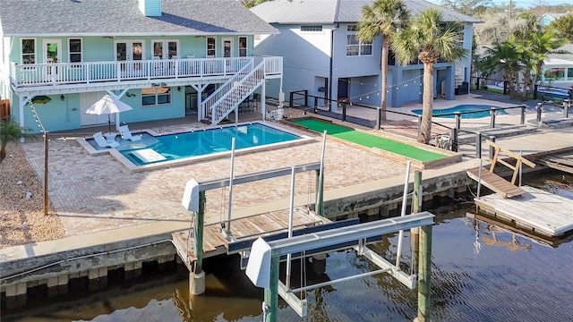 view of pool with a dock, a deck with water view, and a patio