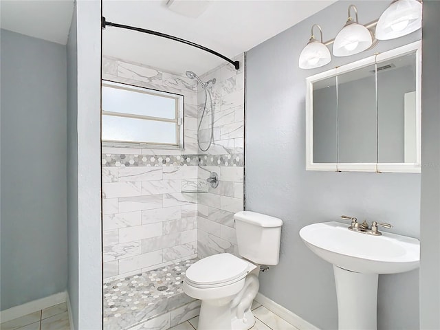 bathroom featuring a tile shower, sink, and toilet